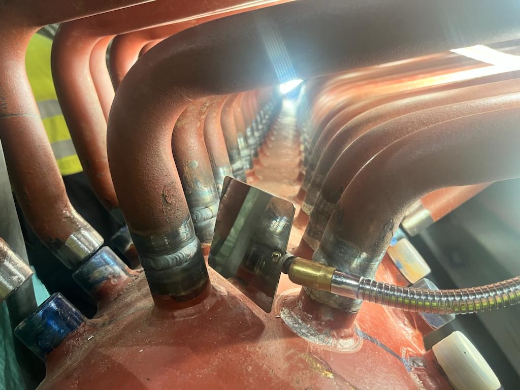 Welder using a mirror to view the weld between boiler tubes